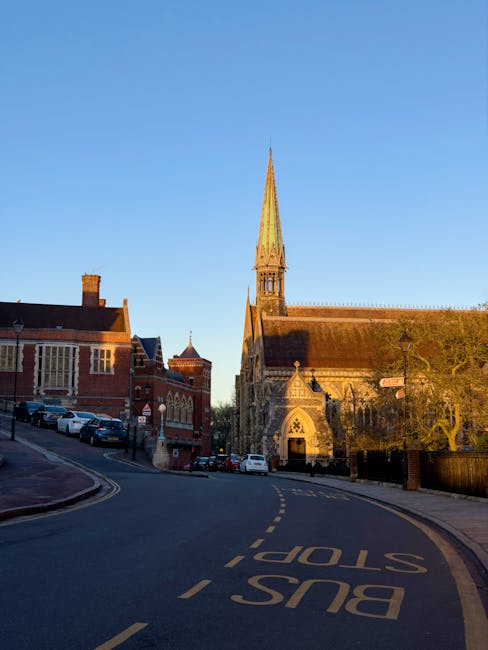 A historic stone church with intricate Gothic architecture and stained glass windows, featuring a tall spire reaching towards the evening sky with a mix of orange and blue hues; in the foreground, the